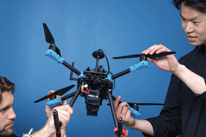 Two people assembling a quadcopter drone against a blue backdrop at Bay Area Drone Fest