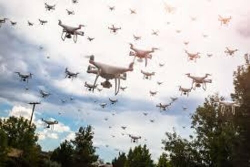 A swarm of small quadcopter drones flying against a cloudy sky