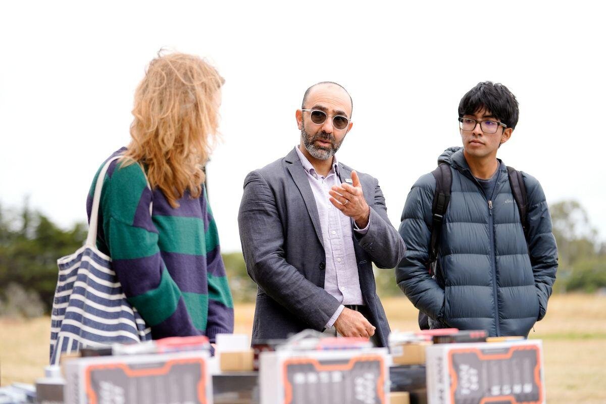A coordinator speaking with students beside a table of drone batteries